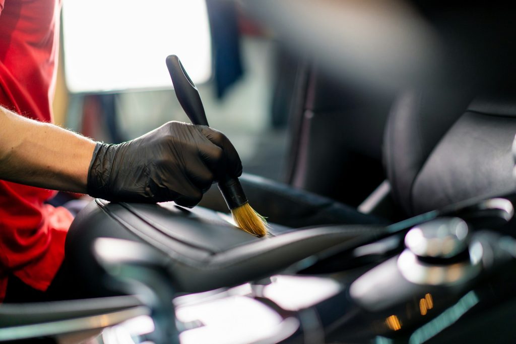 Car wash worker thoroughly cleaning the leather interior of a luxury car with a brush detailing